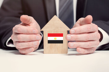 Businessman hand holding wooden home model with Egyptian union flag. insurance and property concepts