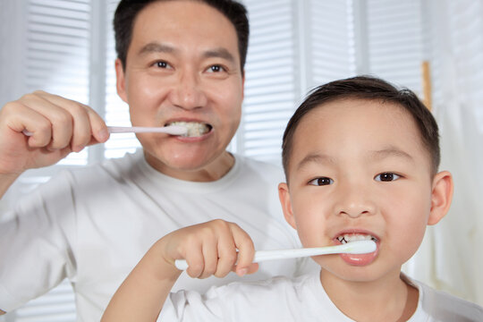 The little boy and his father are brushing their teeth in the bathroom