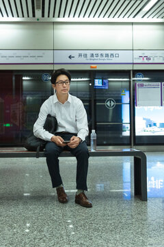 A middle-aged man sitting in a subway station waiting for a bus