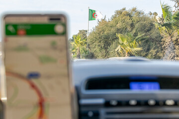 Inside car driver view on Algerian flag pole and trees with blue sky and sunny day on the highway...