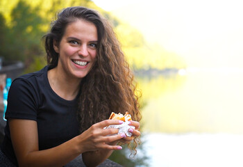 Attractive girl smiling at camera holding hamburger in her hand.