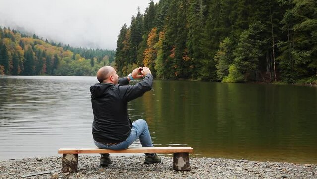 A man on the shore of a mountain lake enjoys the beauty of nature and photographs the landscapes. High quality FullHD footage