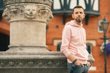 Welcome concept. Young smiling romantic man wearing pink trendy hoodie posing over brick house with...