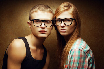 Funny twins concept. Portrait of two gorgeous red-haired fashion models in casual clothing wearing trendy glasses and posing over golden background together. Hipster style. Close up. Studio shot