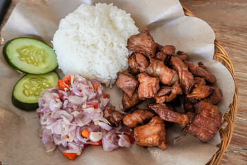 Crispy fried pork served with white rice, sambal matah and sliced cucumber. Balinese mixed rice or nasi campur. Bali authentic delicious food. Concept for bali tourism and culinary.