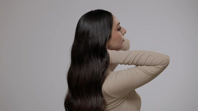 Young charming brunette woman with long wavy hair posing on a light gray background.