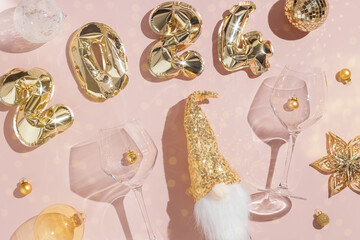 Happy New Year background, golden inflatable balls in form 2024 on pink background, sparkling wine champagne bottle, wine glasses with Christmas holiday shiny decor, top view, flat lay pattern