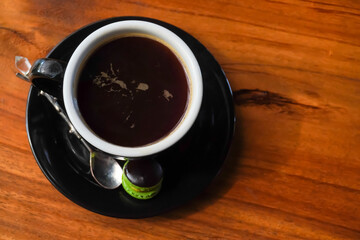 Obraz na płótnie Canvas Hot Black Coffee in a porcelain glass on a wooden table. Morning coffee in ceramic mug with macaron and tea spoon. Concept for breakfast, working, task, job, business plan - High angle photo