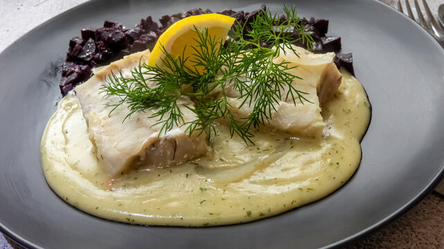 Kochfisch mit Dillso&szlig;e fokussiert angerichtet auf einem schwarzen Teller