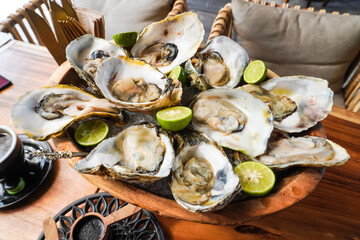 Raw fresh oysters with lime wedges on ice cubes served to seafood restaurant customers in Bali....