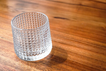 A glass cup with a rough textured outer surface. Transparent clear glass on wooden table. Empty...