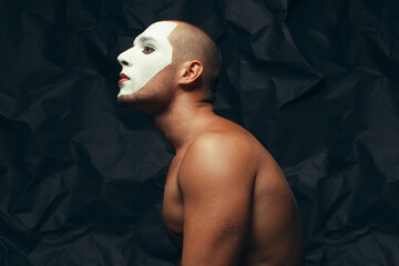 Behind curtains concept. Arty portrait of circus performer over black wrinkled background. White mask on face. Muscular body and perfect tan. Close up. Text space. Studio shot - obrazy, fototapety, plakaty
