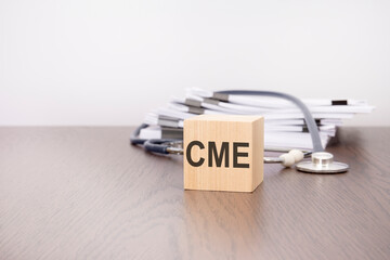 wooden block with black letters CME, stethoscope on gray table. medical and education concept.