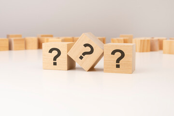 three wooden cubes with question marks over a grey background with copy space