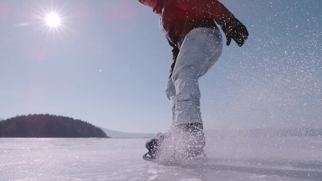 SUPER SLOW MOTION, CLOSE UP: Flying pieces of ice when young guy brakes on skates. Active man is ice skating on a big frozen lake and practicing hockey stop. Beautiful sunny day for winter activities.