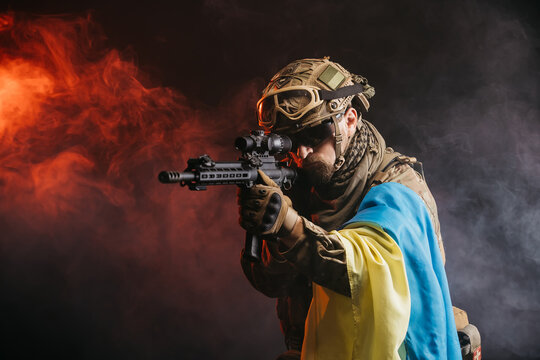 Ukrainian special forces soldier or private military contractor with rifle and Ukrainian flag. Image on a black and red background. The concept of war, army, weapons and computer games.