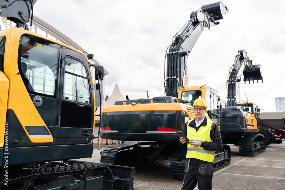 Aufkleber engineer in a helmet with a digital tablet stands next to construction excavators.