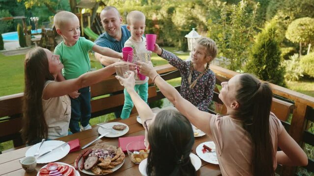 Cheerful family and friends with children are toasting during lunch in the yard at home