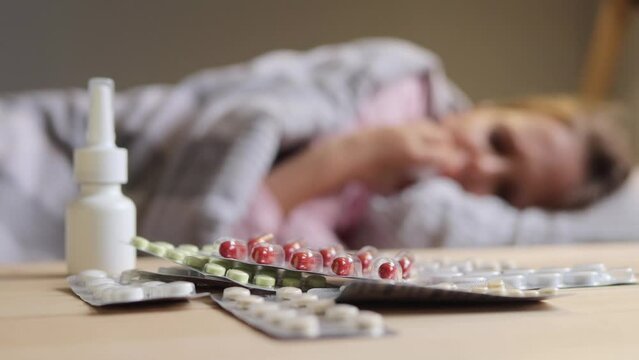 Unwell child. Bronchial disease care. Healthcare recovery. Home sickness medical supplies lying on bedside table beside the bed where sick little girl lying, blurred view.