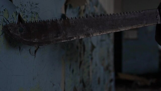 A maniac killer runs a knife blade along an old wall with peeling paint. Scary shot, horror movie