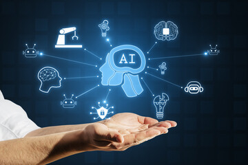 Close up of businessman hand holding creative glowing ai hologram with digital human head on dark background. Machine learning, artificial intelligence and conversation assistant concept.