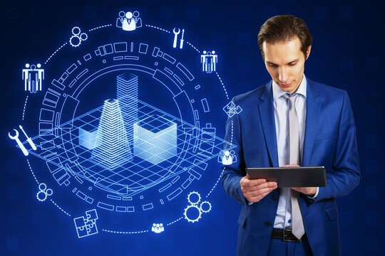 Attractive young european businessman using tablet with creative digital architectural project, round wireframe sketch with icons on blue background. Real estate, VR and model concept.