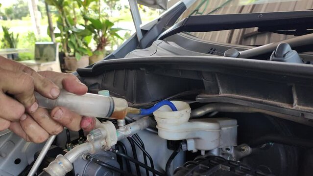 Motor Car Mechanic uses a straw to suck car brake fluid out of the tank to change the brake fluid. Concepts of car care and safety inspection of the brake system.