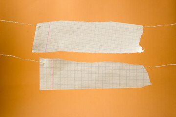 Torn paper hanging on a rope on an orange background. Two sheets of paper hang on a rope. Concept: announcement, reminder