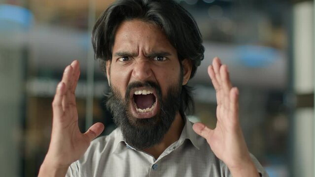 Close-up emotional angry aggressive furious displeased stressful irritated mad Indian bearded man guy shouting screaming yelling swearing shout scream looking at camera stressed male portrait indoors