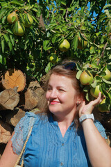 Portrait of a young woman standing under a tree with ripe pears.