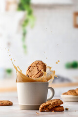 Cookies fall into a cup of hot coffee or cocoa on light kitchen background. Levitation of food. Copy space