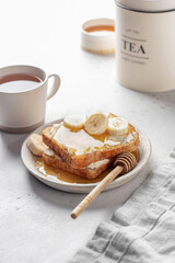 Toasts with butter, banana slices and honey on light kitchen background. Homemade breakfast sandwich. Healthy vegan food concept