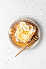Toasts with butter, banana slices and honey on light background. Homemade breakfast sandwich close up with text space. Simple food. Top view