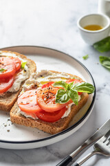 Fototapeta na wymiar Sandwiches or toasts with tomatoes, cream cheese, olive oil and basil on a plate on white marble background. Traditional italian mediterranean food