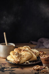 Crepes or thin pancakes with honey and nuts on brown plate over wooden background. Delicious...