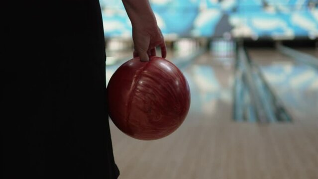 Bowling ball in female hand before throw indoor closeup. Woman holds standard heavy pearl colored ball in front of ready free lane, preparing to knock down pins.