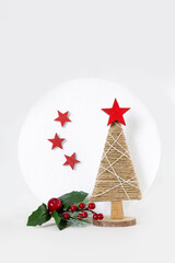 Simple Christmas tree made with strings on white background. Stars are made of red wood. Wooden base. There's sprig of holly and white moon behind tree. Vertical.
