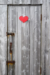 Rustic wooden door on with rusty hardware, red wood heart symbolizing an outhouse
