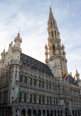 Fototapeta na wymiar Sweeping View of Brussels Town Hall with Clock Tower and Trio of Flags - Grand Place's Gothic Jewel