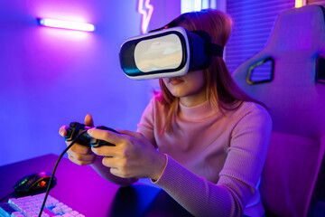 Gamer in VR headset glasses exploring metaverse play video game online with joystick on computer neon lights, Excited woman virtual playing gamepad controller she very determined at home
