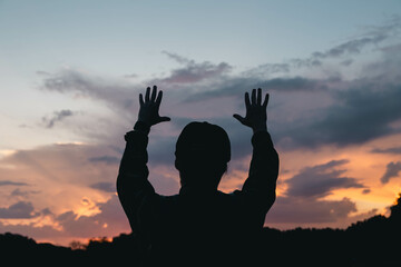 A young Christian man with a beard in nature raises his hands to the sky, thanks God, praises.