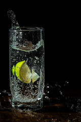 Gin tonic cocktail with lime slice  in a glass splash on black background