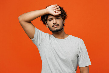 Young sad sick ill exhausted tired unhappy upset Indian man he wears t-shirt casual clothes hand on forehead looking camera isolated on orange red color background studio portrait. Lifestyle concept. - Powered by Adobe