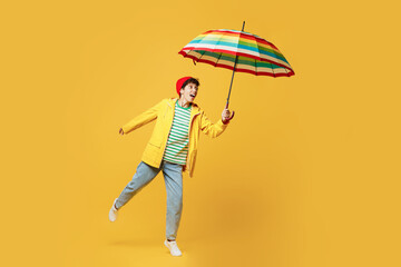 Full body young happy woman wears waterproof raincoat outerwear red hat hold run with umbrella isolated on plain yellow background studio portrait. Outdoors lifestyle wet fall weather season concept.
