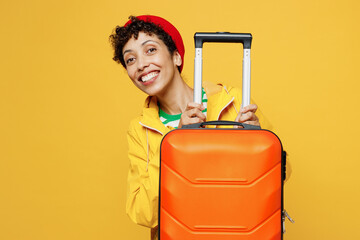 Traveler smiling woman wear waterproof raincoat outerwear hold bag suitcase isolated on plain...