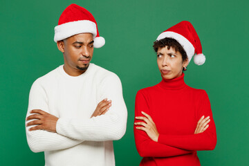 Merry young couple man woman wearing red casual clothes Santa hat posing hold hands crossed folded look to each other isolated on plain green background. Happy New Year 2024 Christmas holiday concept.