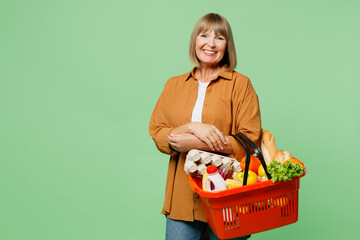 Side view elderly smiling happy cheerful woman wear brown shirt casual clothes hold shopping basket...
