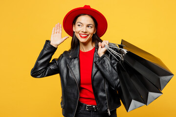 Young curious nosy woman wear casual clothes red hat hold shopping paper package bags try to hear you overhear listening intently isolated on plain yellow background Black Friday sale buy day concept