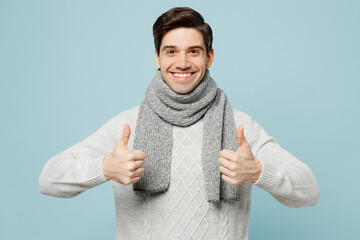 Young smiling happy ill sick man in gray sweater scarf show thumb up gesture isolated on plain blue...