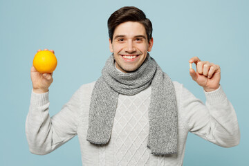 Young ill sick man wear gray sweater scarf hold in hand lemon and capsule pill isolated on plain...
